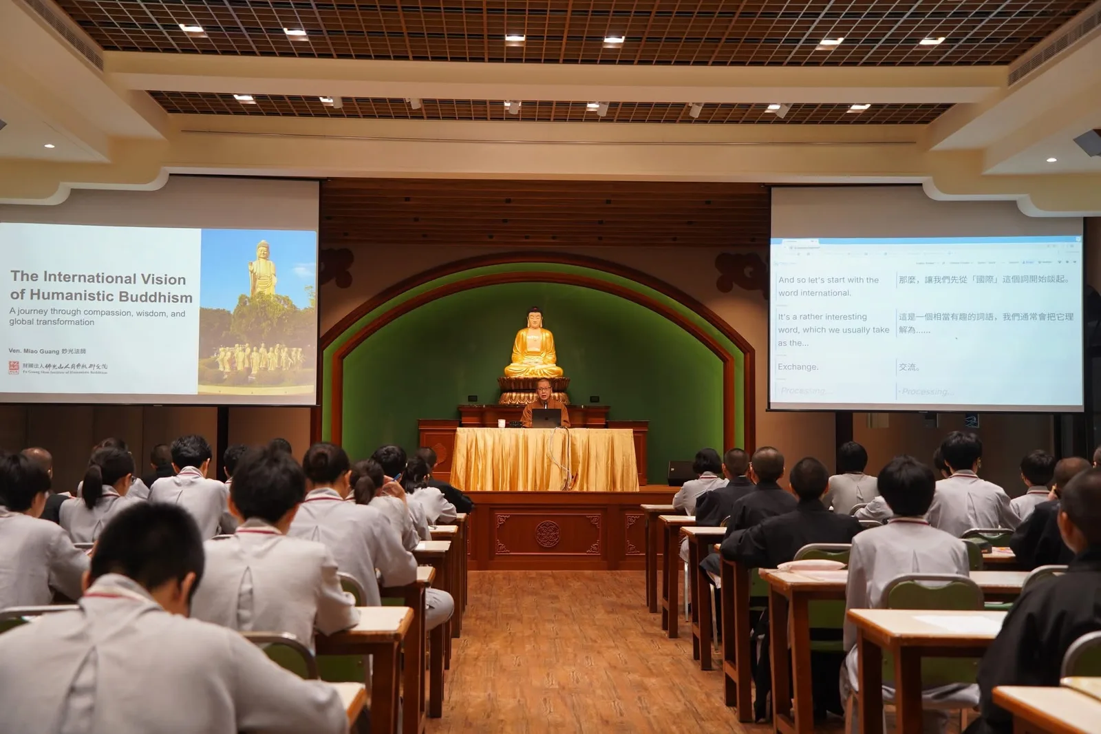 A monastic teaching beneath the golden Buddha in a Fo Guang Shan hall, with Orato Flow’s live bilingual captions on the screen beside the slides.