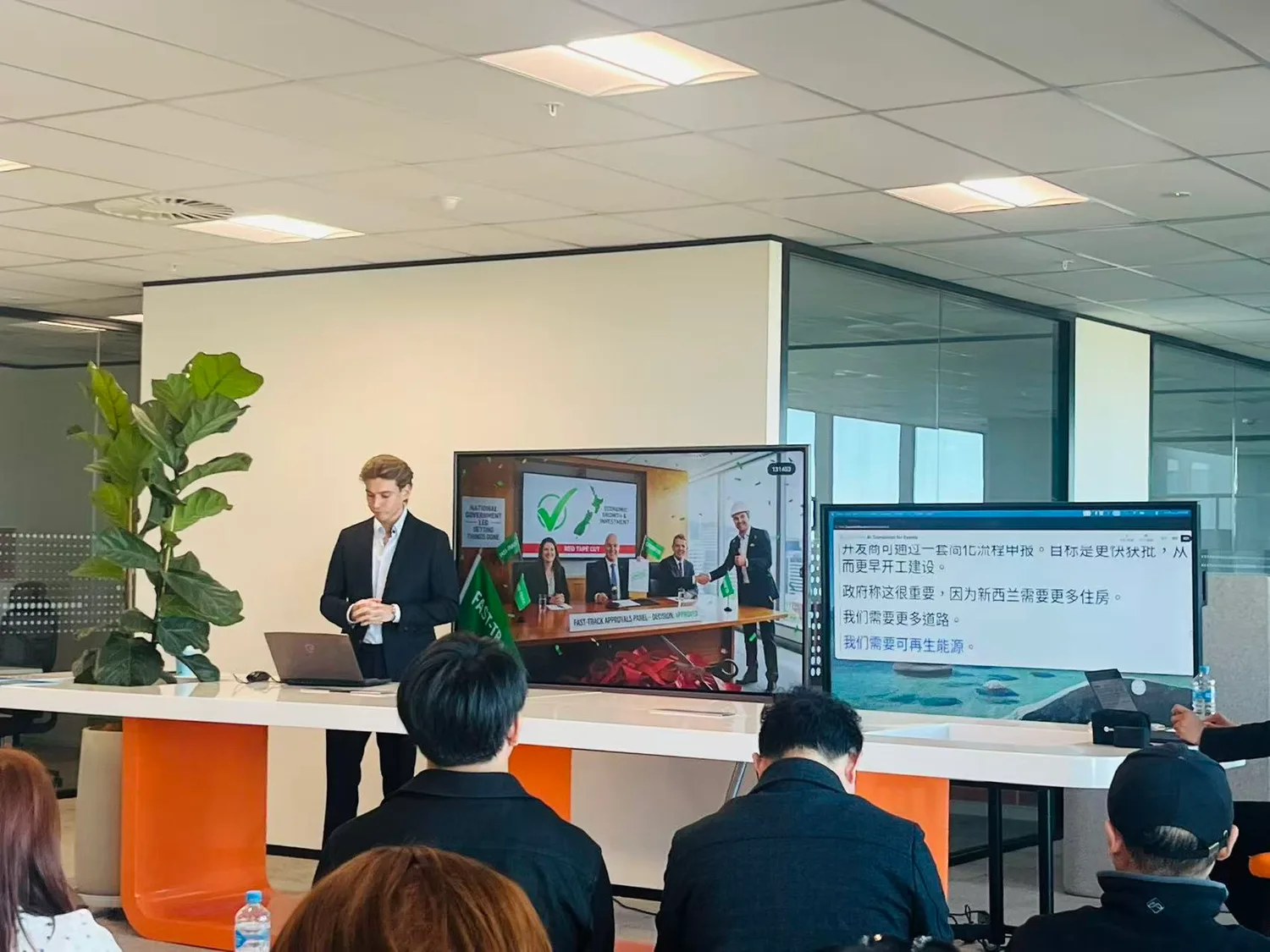A My Land presenter beside the Fast-track Approvals slide, with Orato Flow’s live Chinese translation on the screen alongside it.