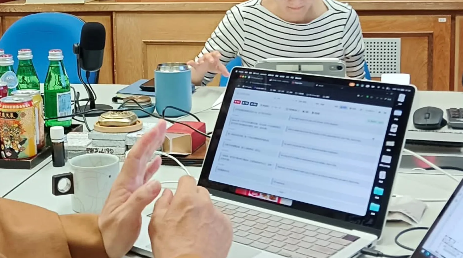 A close view of the meeting table: a microphone, a laptop showing Orato Flow’s bilingual transcript, and a floor plan open on a tablet.