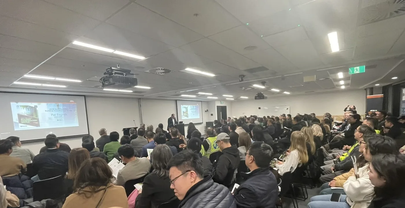 A packed training room at Mitre 10 Albany seen from the back, with the report launch presentation on the projector screen at the front.