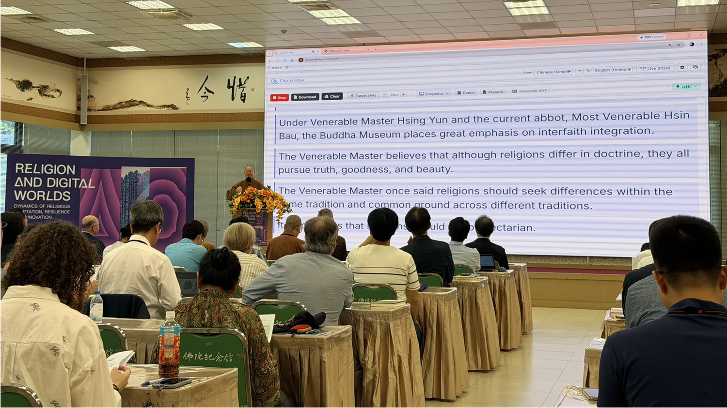 A speaker at the Religion and Digital Worlds symposium with Orato Flow English captions on the main screen.