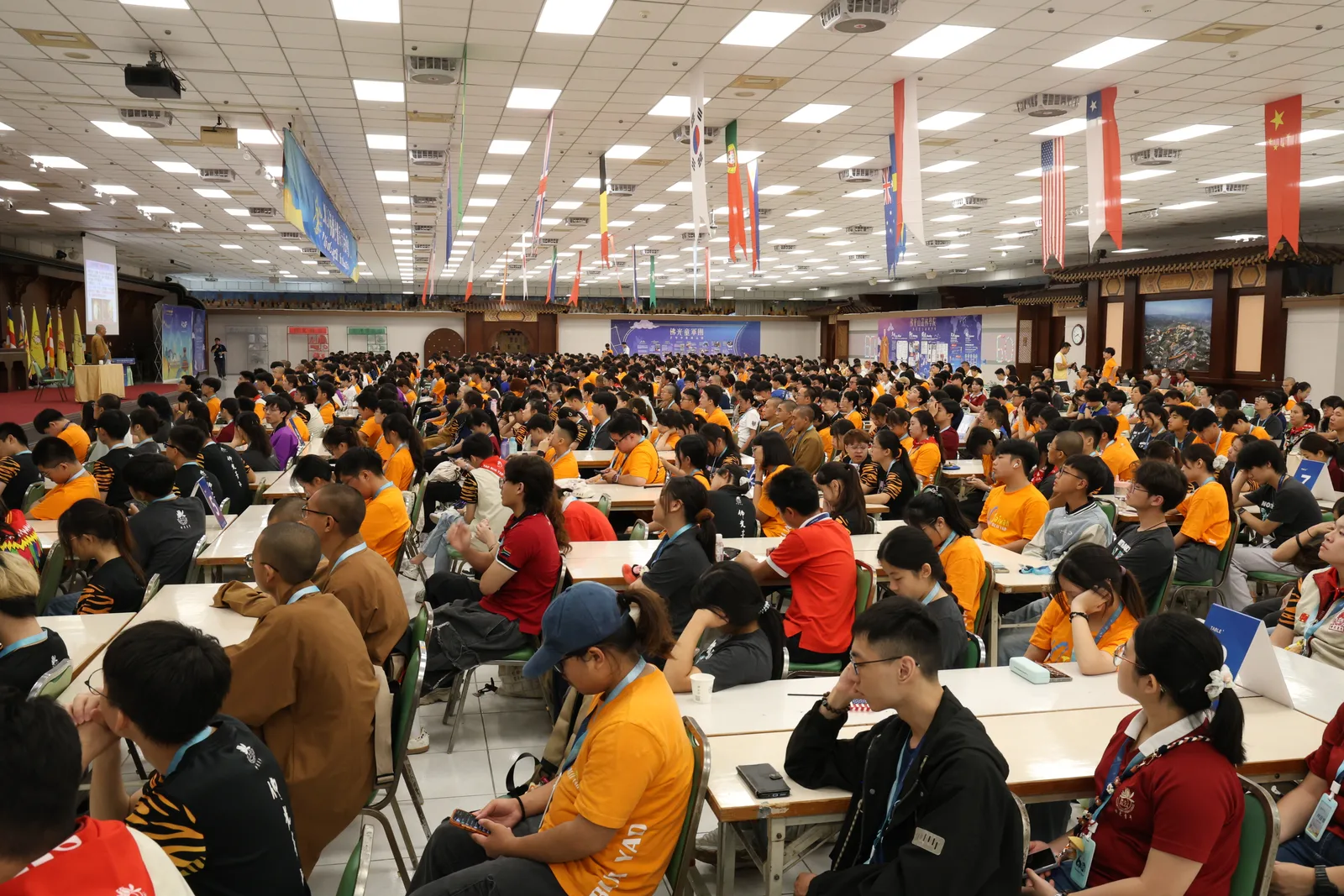A packed hall of youth delegates at the 2026 Fo Guang Shan Youth Summit, with the national flags of a dozen countries hanging overhead.