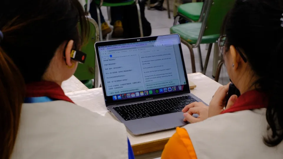 Two young delegates read Orato Flow’s live transcript on a laptop — source speech and translation side by side.