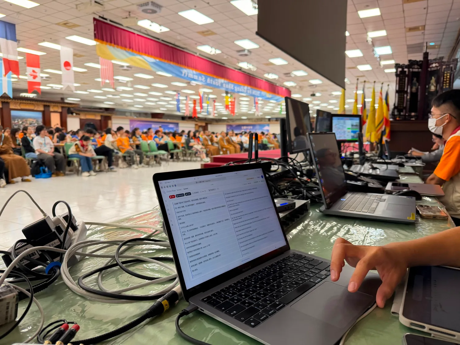 An operator running Orato Flow on a laptop while delegates sit beneath rows of international flags.
